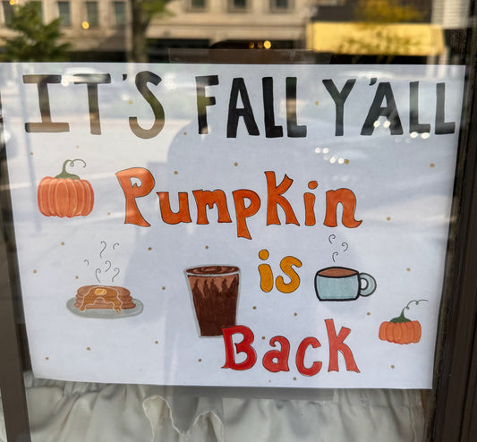 A sign in a window that says "it's fall y'all. pumpkin is back"